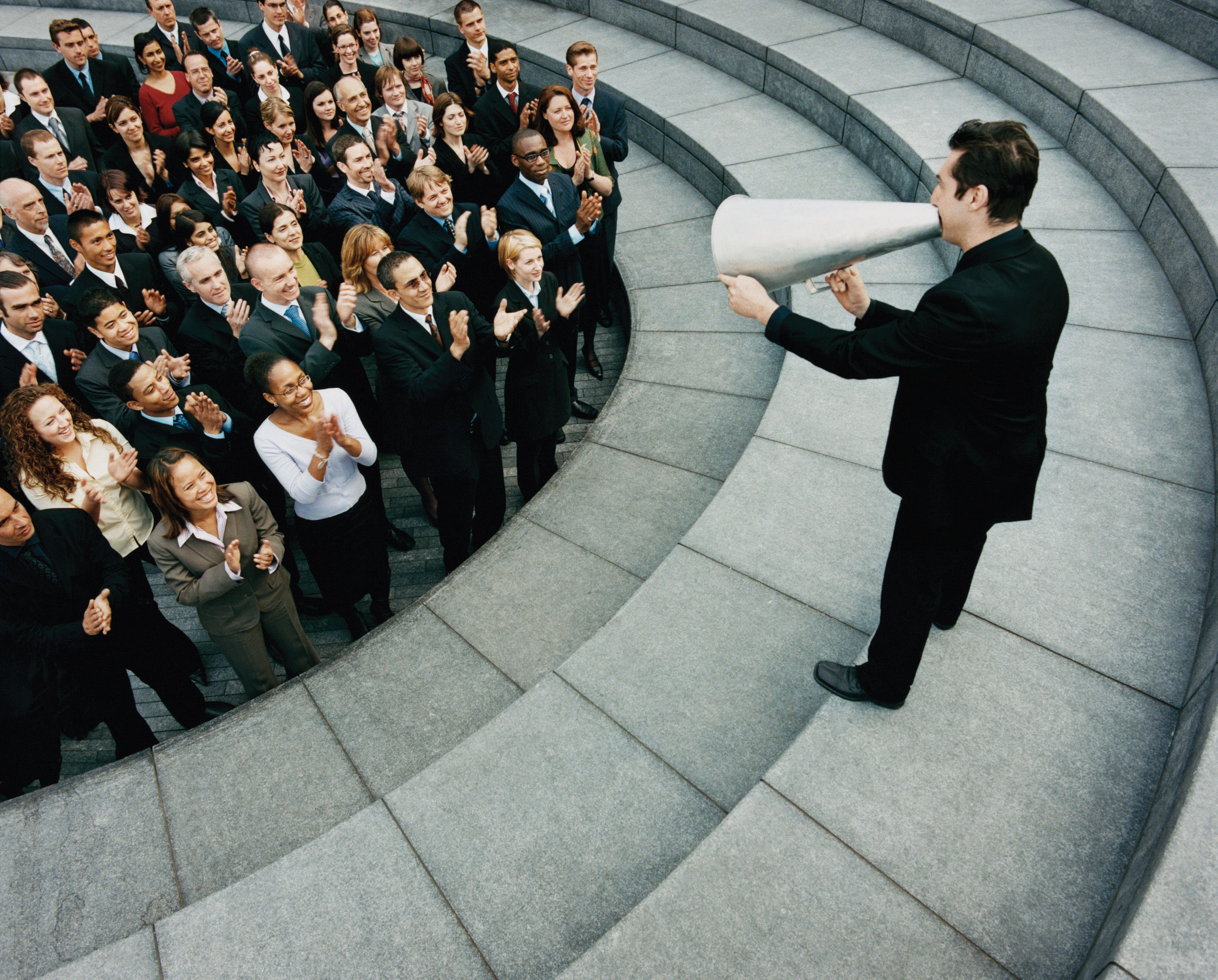 A crowd applauding a man using a cone to amplify his voice