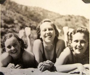 A black and white photo from the 1930s of three young women on the beach smiling for the camera.