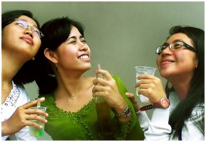Three women posing with smiles and drinks.